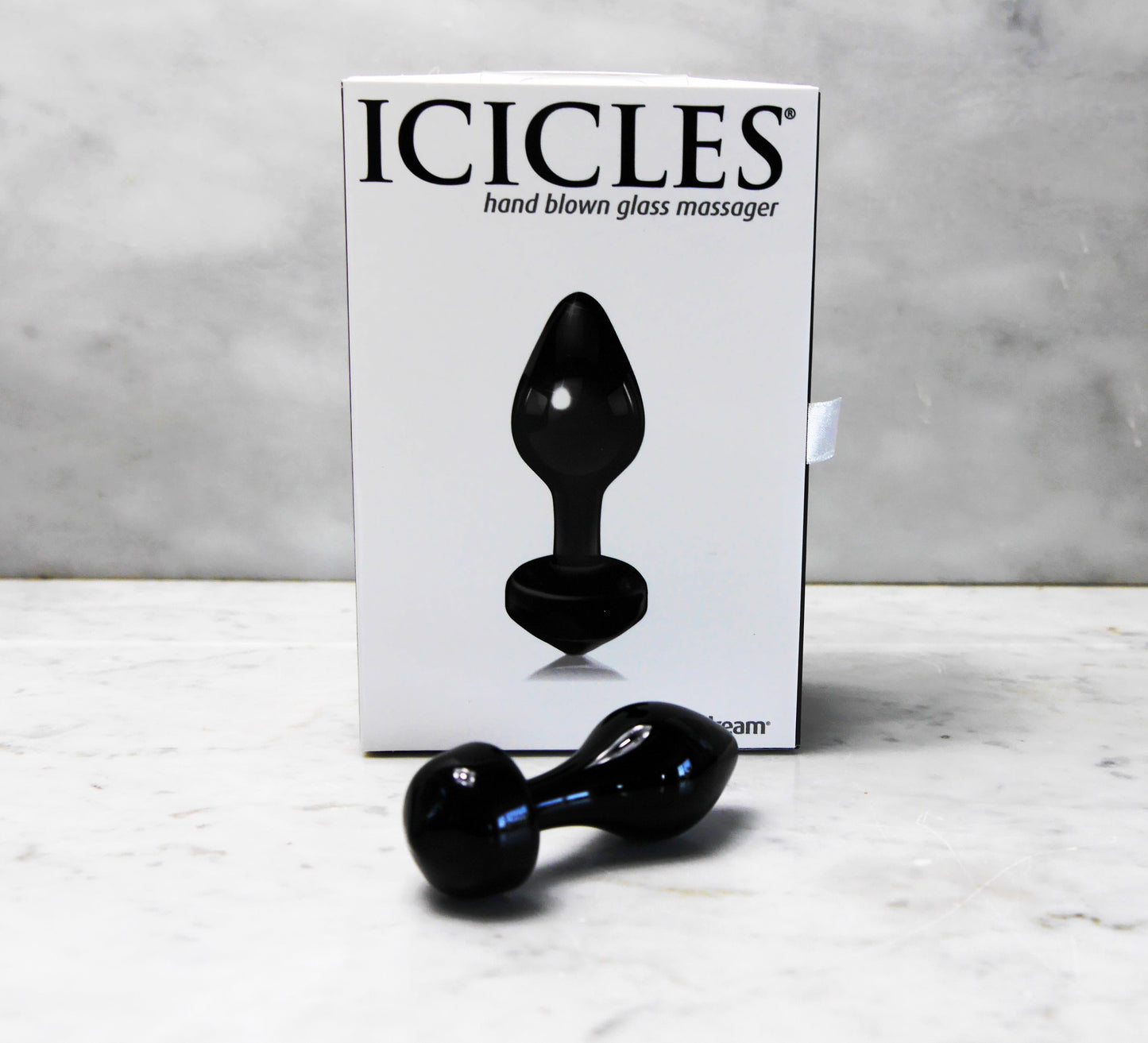 Handgeblazen glazen buttplug Icicles, zwart, met witte verpakking op marmeren ondergrond.