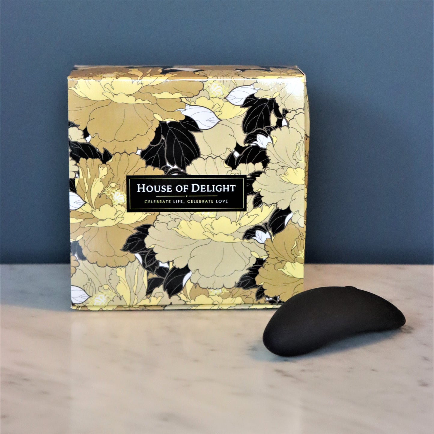 Zwarte Aludra stimulator naast luxe geschenkverpakking met gouden bloemenprint