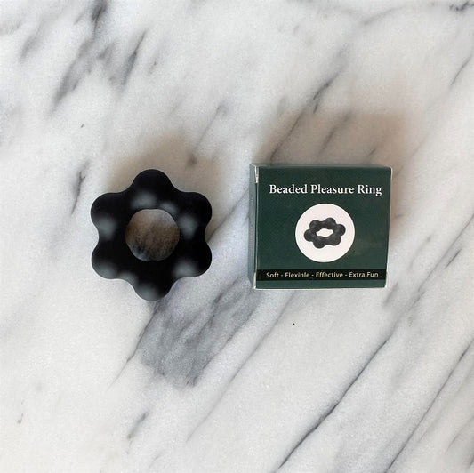 Beaded Pleasure Ring cockring in zwart met bloemvormig ontwerp naast verpakking