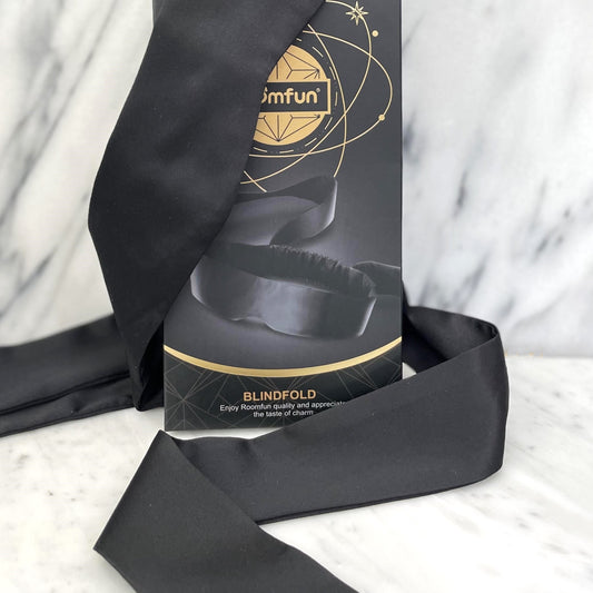 Roomfun luxe blinddoek naast zwart-gouden verpakking op marmer met satijnen linten