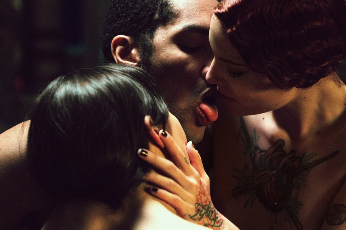 Passievolle close-up van drie getatoeëerde personen die elkaar intiem kussen in warm roodgetint licht